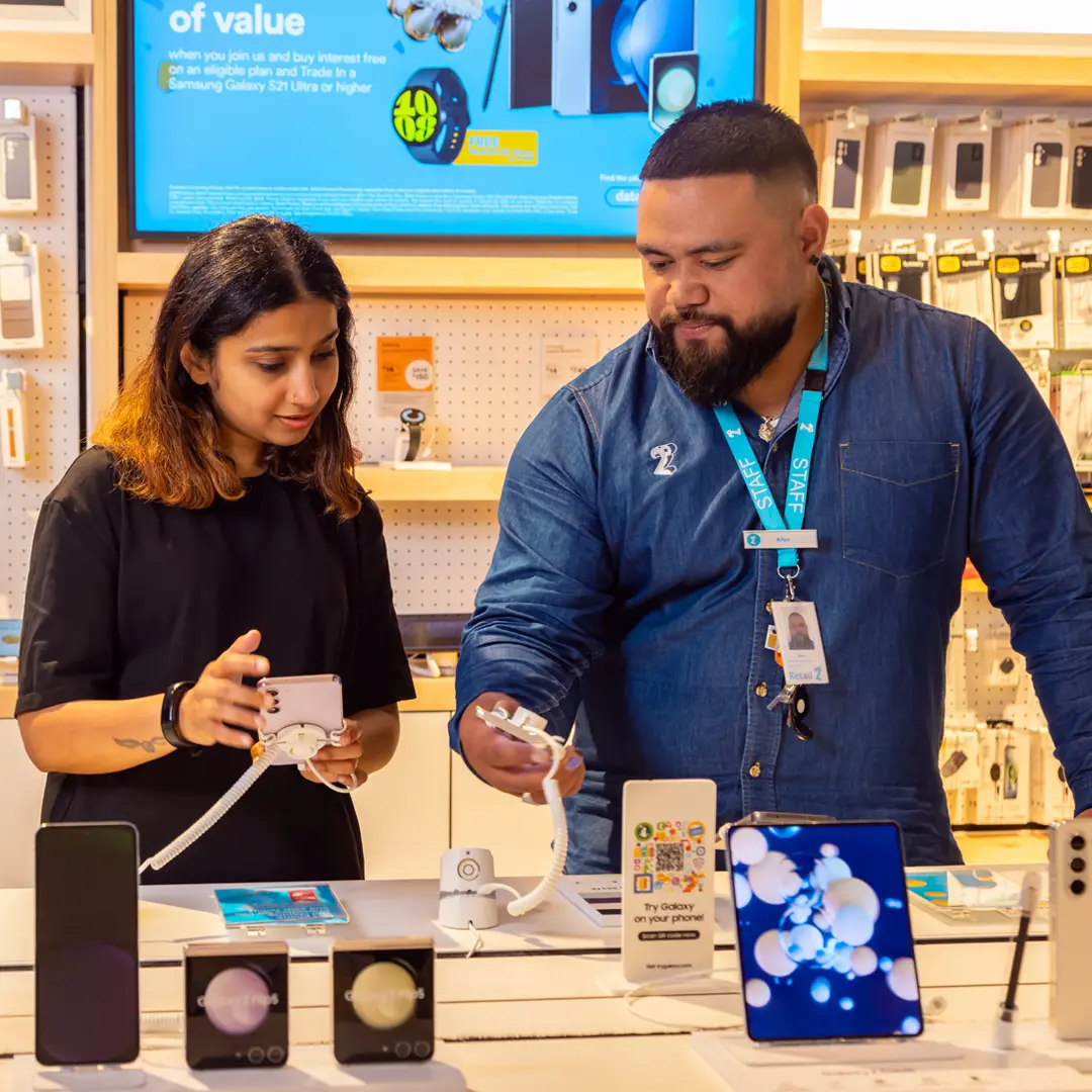 Customer viewing a smartphone with assistance from a 2degrees staff member in a retail store.