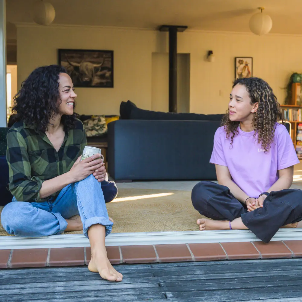Two people sitting on the floor indoors, smiling and talking to each other.
