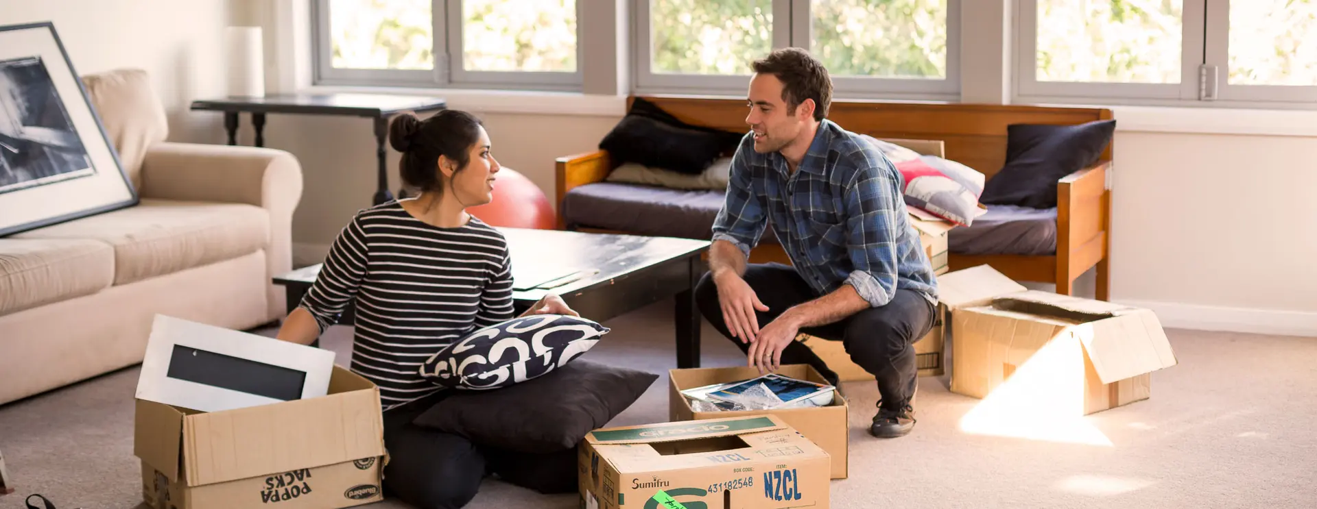 Two people unpack boxes together in a living room after moving house.