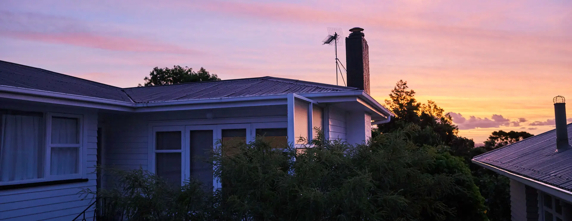 A house at dusk with a purple and orange sunset sky above the roofline.