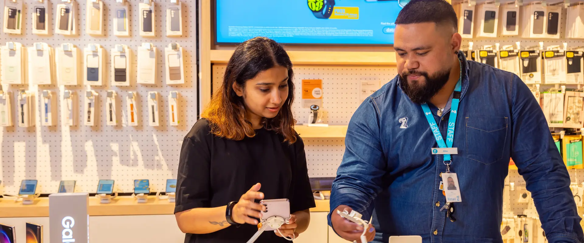 Customer viewing a smartphone with assistance from a 2degrees staff member in a retail store.