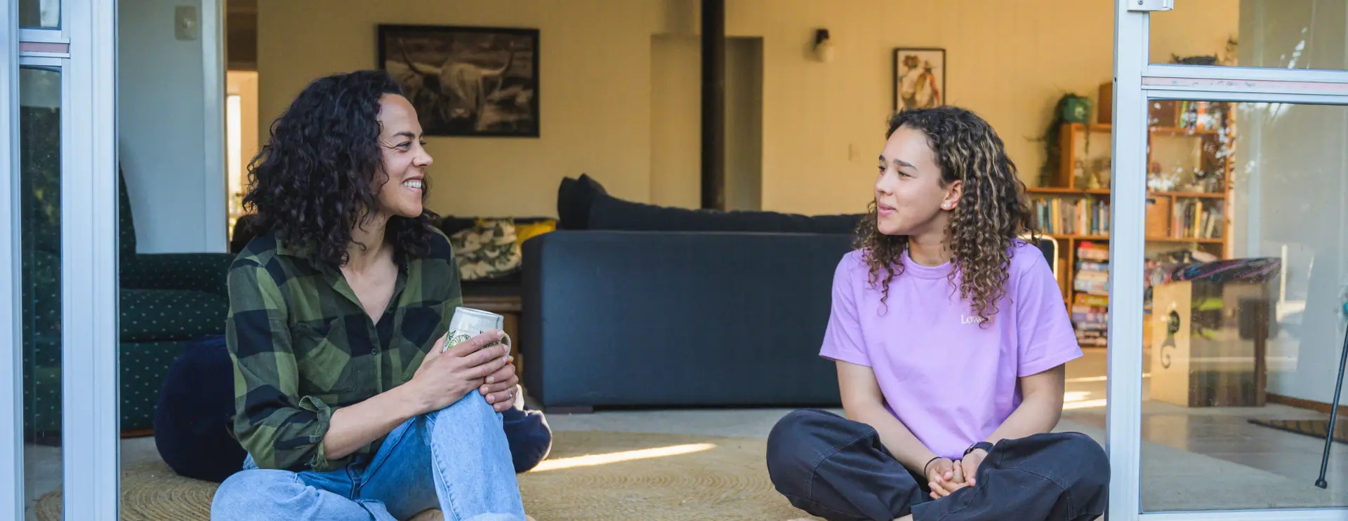 Two people sitting on the floor indoors, smiling and talking to each other.