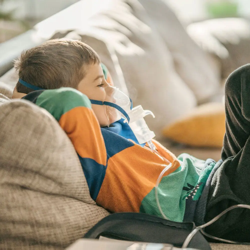 A child lying on a couch wearing a breathing mask connected to medical equipment.