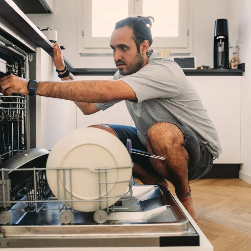 Man crouched down, looking into an open dishwasher