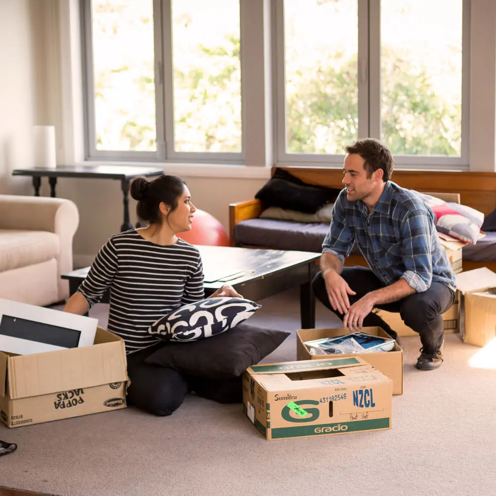 Two people unpack boxes together in a living room after moving house.