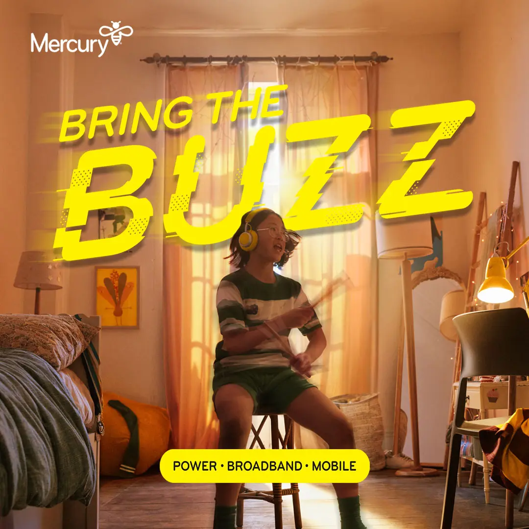 Young person wearing headphones and playing drumsticks while sitting in a bedroom.