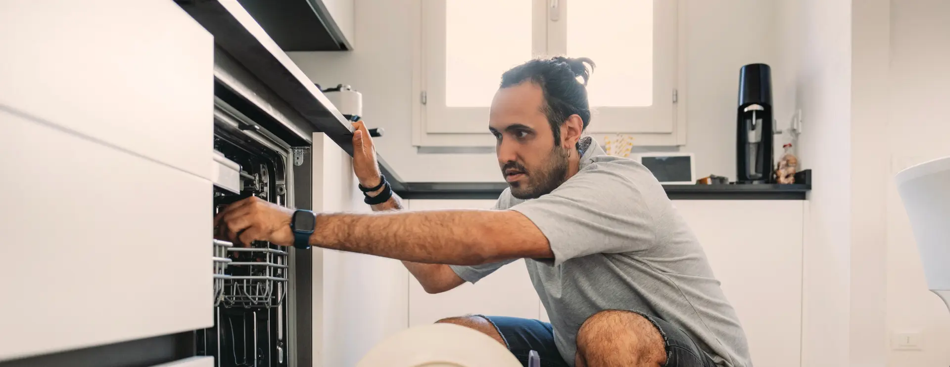 Man crouched down, looking into an open dishwasher