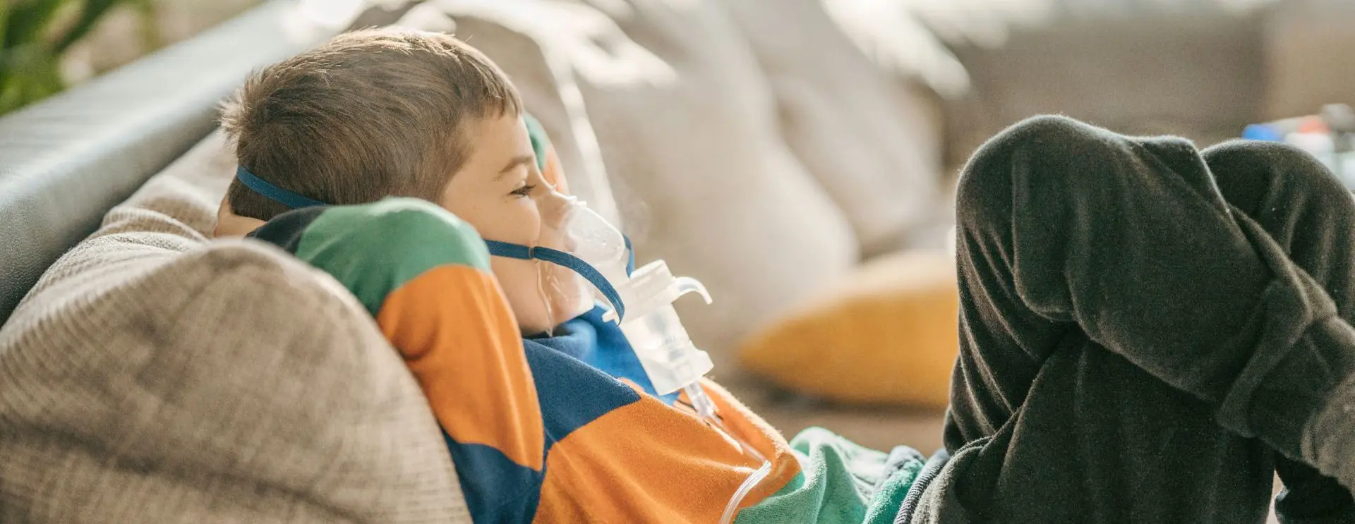 A child lying on a couch wearing a breathing mask connected to medical equipment.