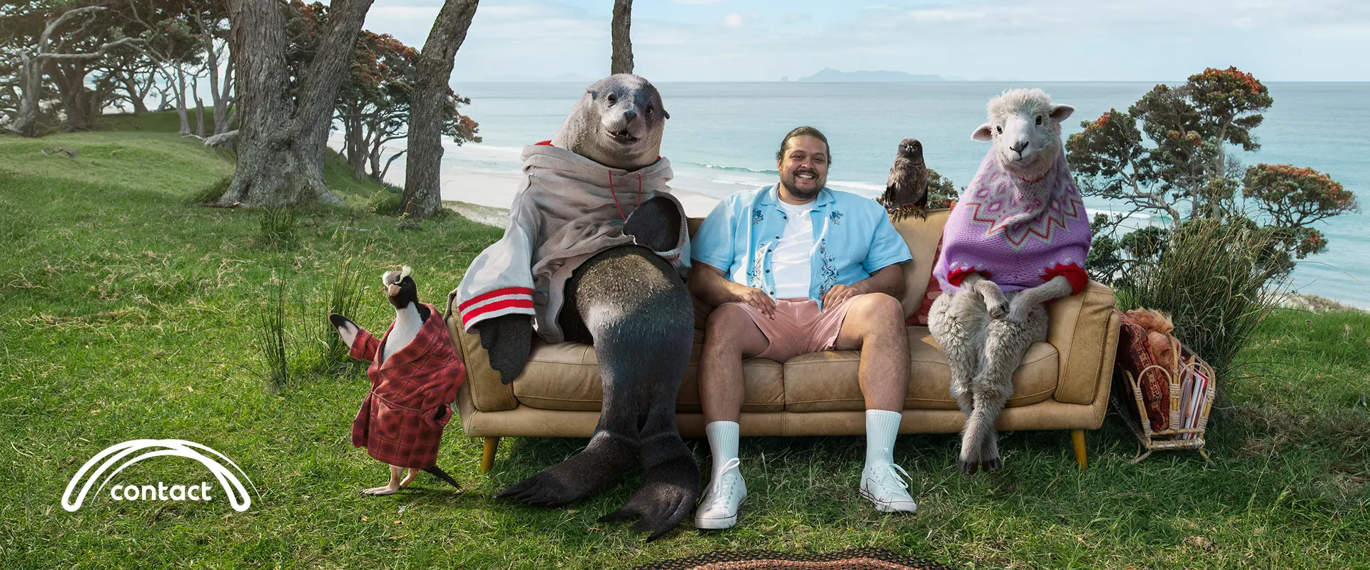 Person sitting on an outdoor couch with costumed animals in a coastal landscape.