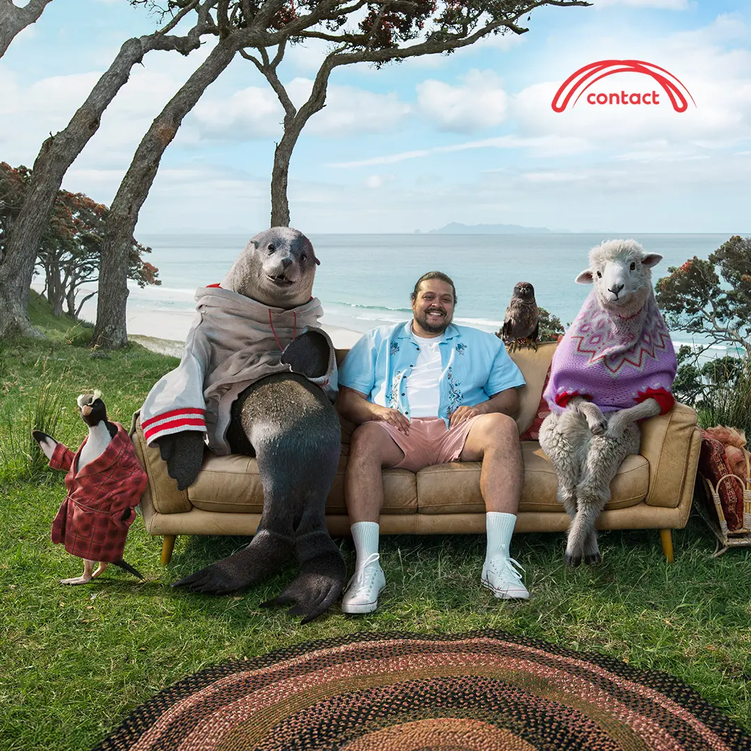 Person sitting on an outdoor couch with costumed animals in a coastal landscape.