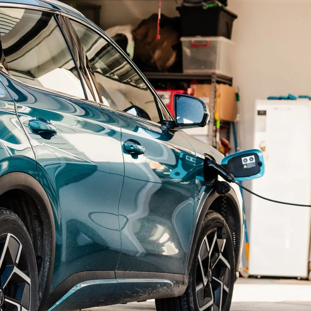 Close-up of an electric car plugged into a home charging unit in a garage.